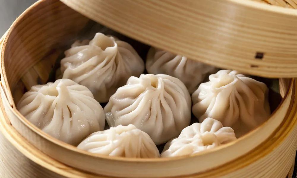 Steamy soup dumplings with pleated wrappers inside open bamboo steaming basket at 88Baobao, a Chinese restaurant in Lubbock.