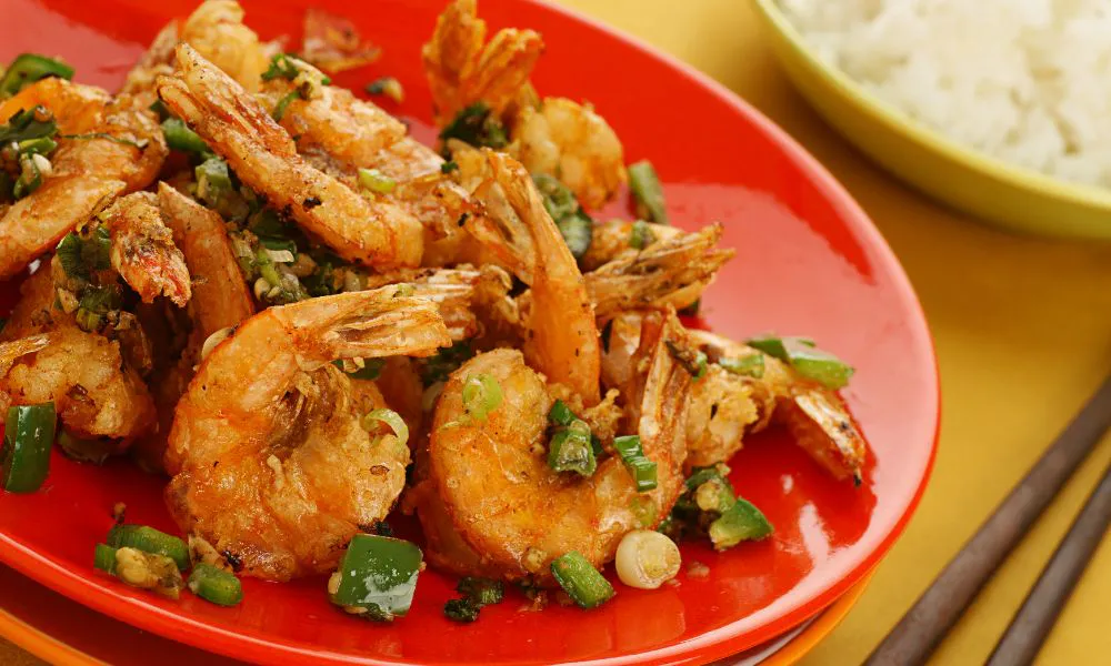 Crispy salt pepper shrimp garnished with chopped green onion on bright red round plate at 88Baobao, a Chinese restaurant in Lubbock.