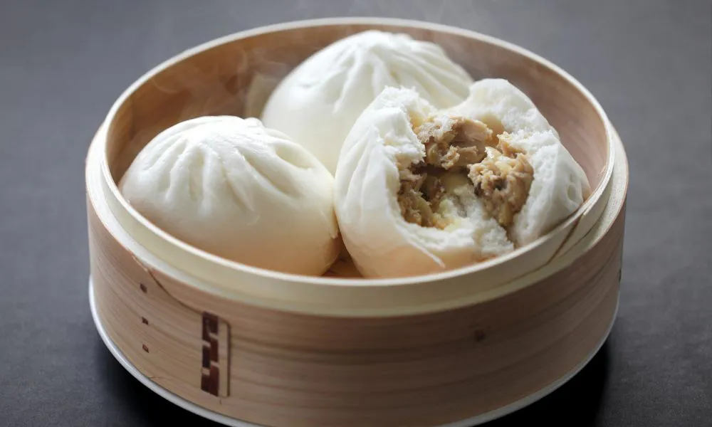 Steamed pork buns in bamboo basket, one split open to show tender meat filling at 88Baobao, a Chinese restaurant in Lubbock.