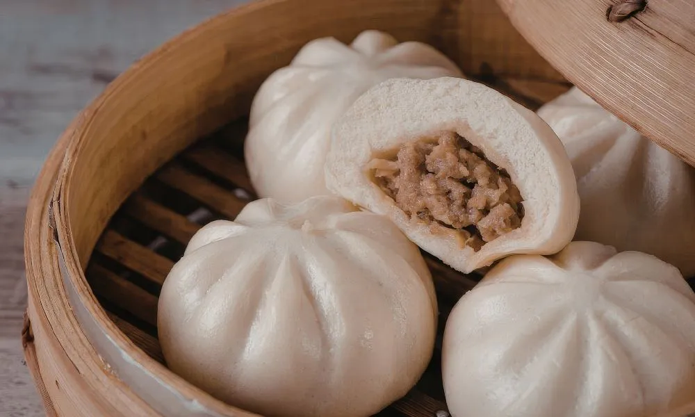 Steamed pork buns in bamboo steamer, one split open to show savory meat filling at 88Baobao, a Chinese restaurant in Lubbock.